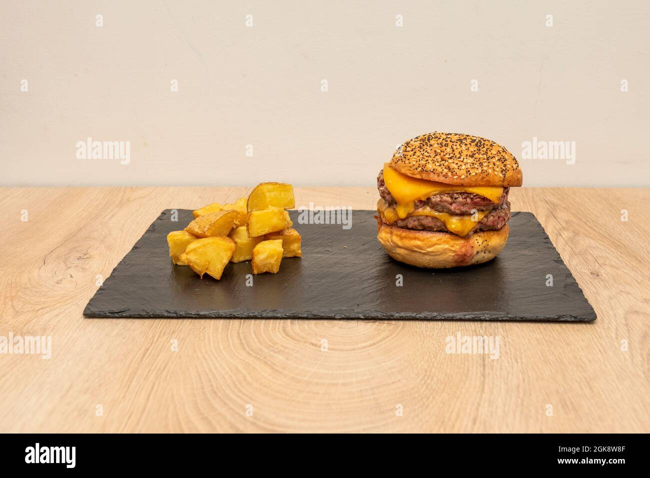 Double Beef Burger mit viel geschmolzenem Cheddar-Käse und gewürfelten pommes auf schwarzem Schieferteller Stockfoto