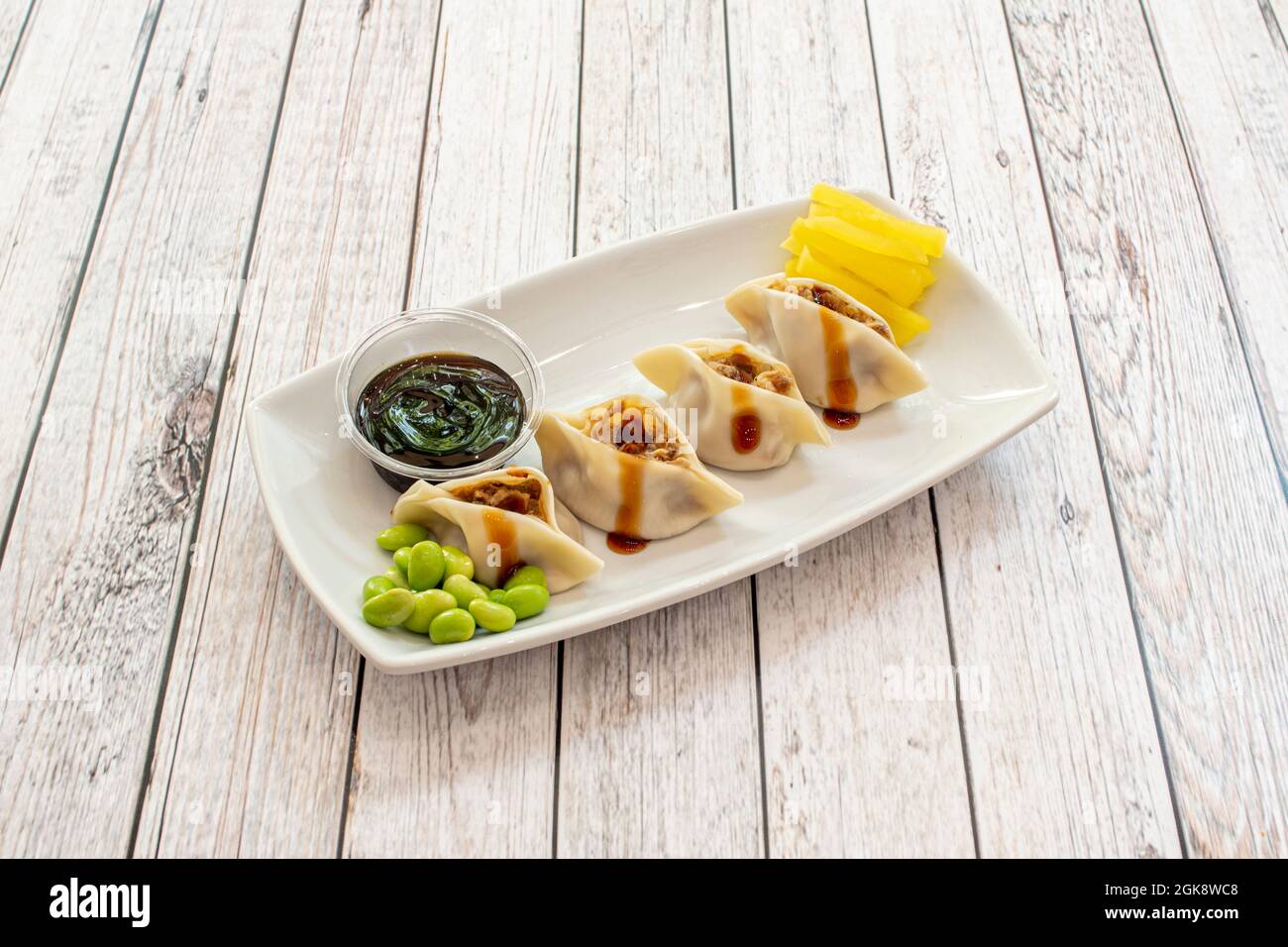 Asiatische Knödel gefüllt mit Fleisch mit Sojasauce und Edamamabohnen, geriebener gelber Pfeffer auf einem weißen Tablett Stockfoto