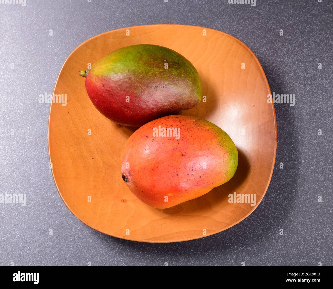 Zwei bunte Mangos und ein Holzteller Stockfoto