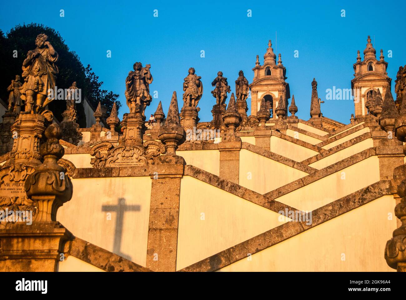 Zickzack-förmige Treppe der Kirche mit zahlreichen verschiedenen Statuen und einem Kreuzschatten - Bom Jesus do Monte, Braga, Portugal, Vertical Stockfoto