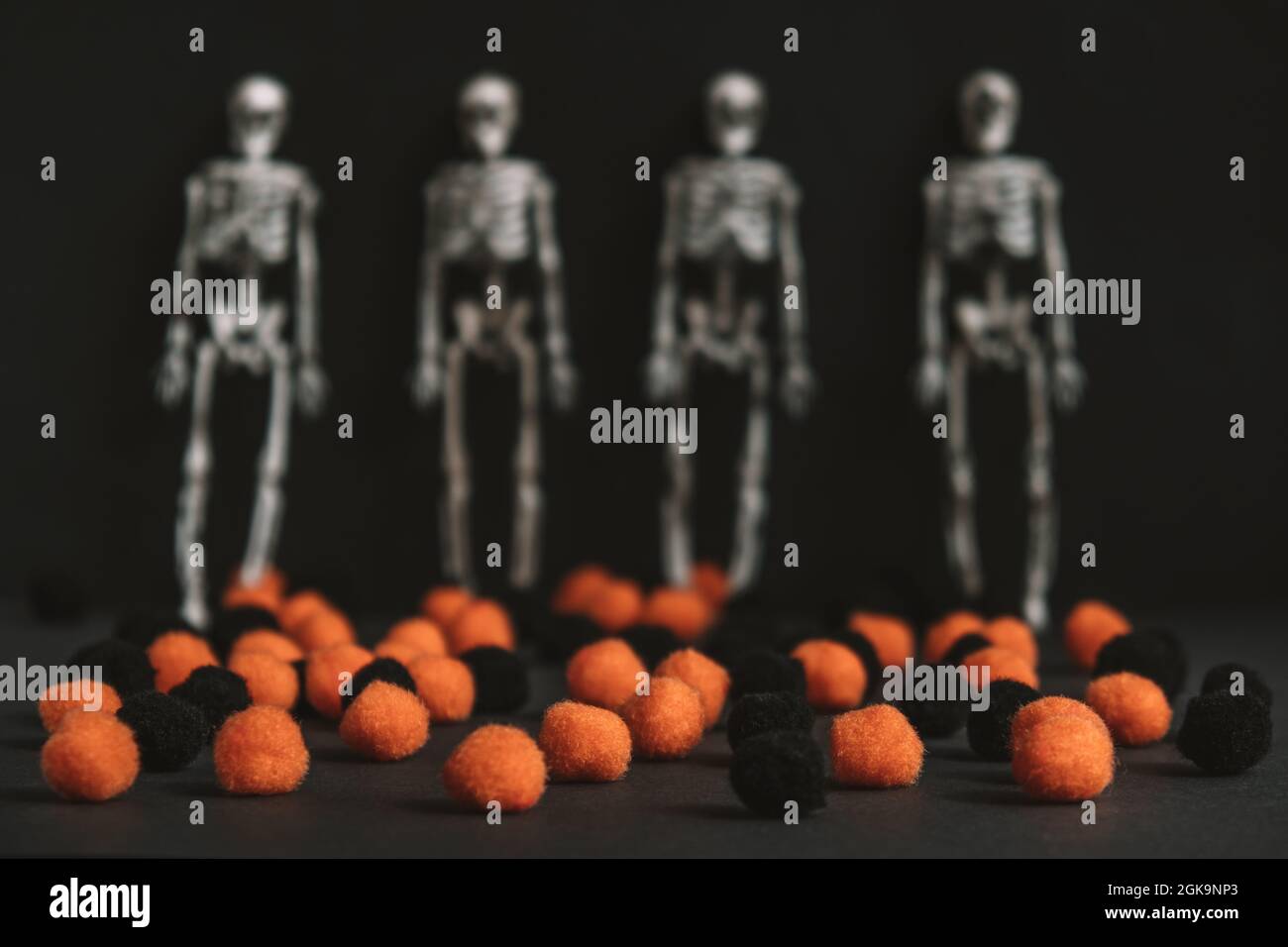 Vorbereitung für Halloween-Party. Schwarze und orangefarbene kleine Kugeln werden zufällig auf einem schwarzen Hintergrund mit unscharfen Skeletten verstreut. Modernes Halloween. Stockfoto