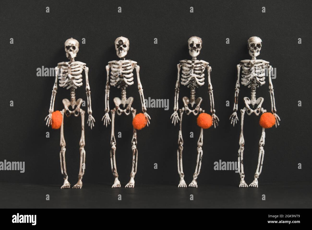 Vier Skelette stehen vor schwarzem Hintergrund und halten kleine orangefarbene Kugeln fest.Vorbereitung für die Halloween Party.modernes Halloween oder Day of the Dead Konzept. Stockfoto