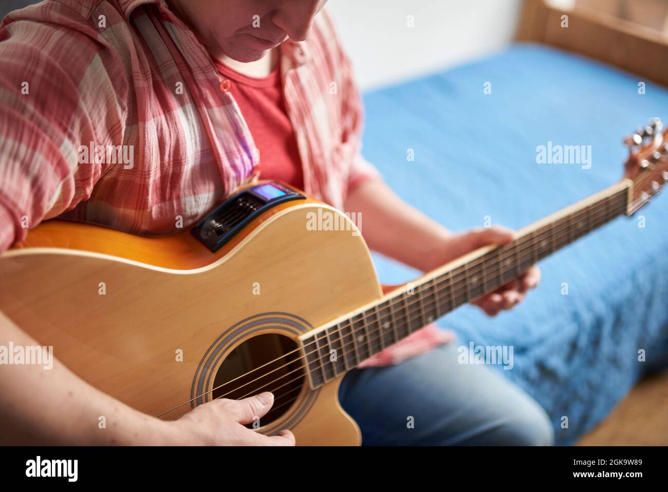 Nicht erkennbarer junger Mann, der zu Hause eine elektroakustische Gitarre stimmt. Stockfoto