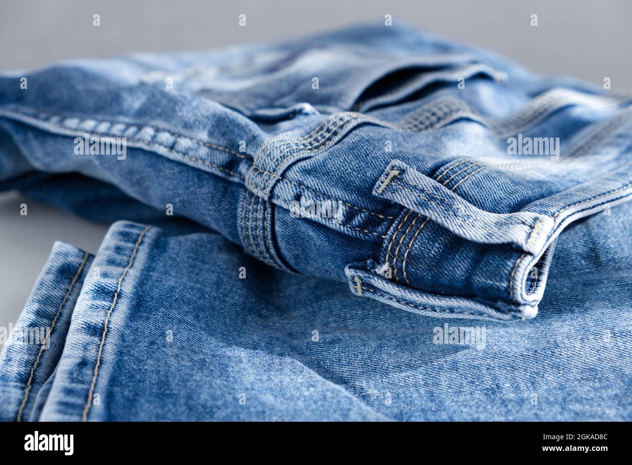 Eine blau-leichte Jeans auf grauem Hintergrund. Nahaufnahme. Sonnenlicht Stockfoto