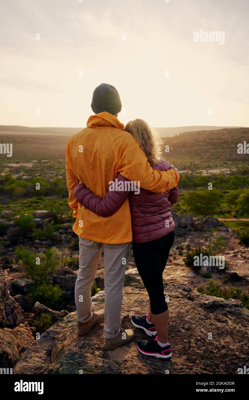 Rückansicht eines verliebten jungen Paares mit Blick auf den wunderschönen Sonnenaufgang am Rand der Bergklippe Stockfoto