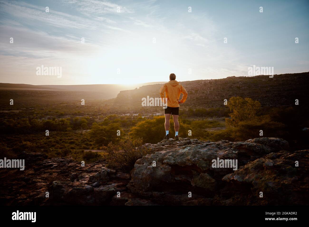 Rückansicht eines jungen Athleten, der nach dem morgendlichen Lauf auf einer Bergklippe steht und den wunderschönen Sonnenaufgang beobachtet Stockfoto