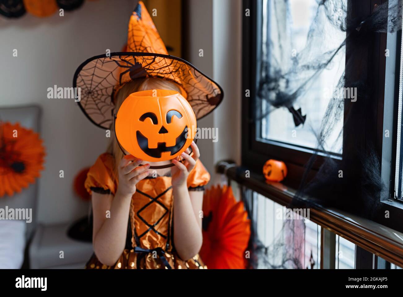 Gruseliges kleines Mädchen im Hexenkostüm, Hut mit großem Kürbis, der  Halloween-Urlaub feiert. Sitzend auf Sessel im Mantel mit Kürbis.  Stilvolles Bild. Horro Stockfotografie - Alamy