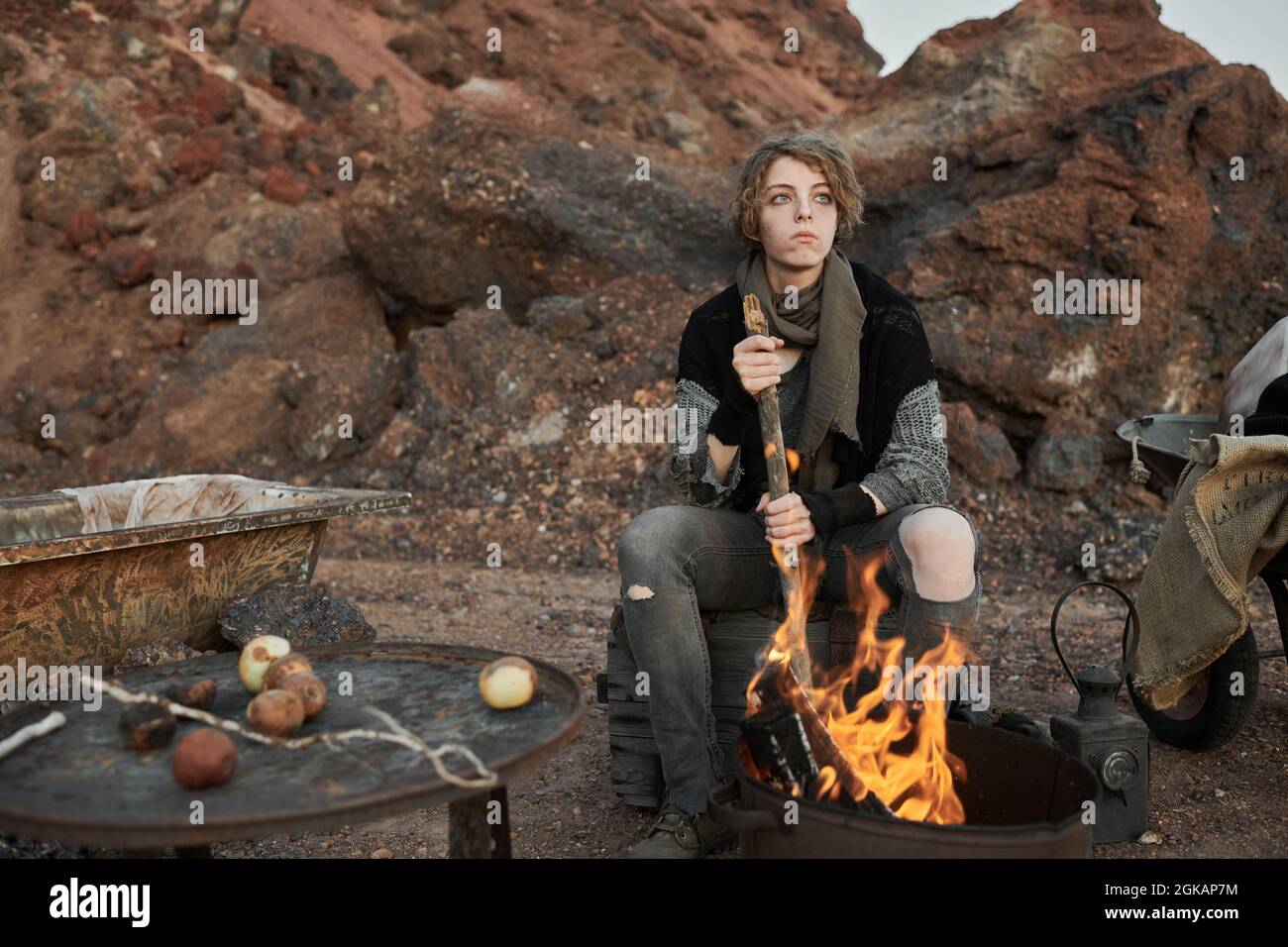 Junge obdachlose Frau, die vor dem Feuer sitzt und das Essen draußen für sich selbst kocht Stockfoto