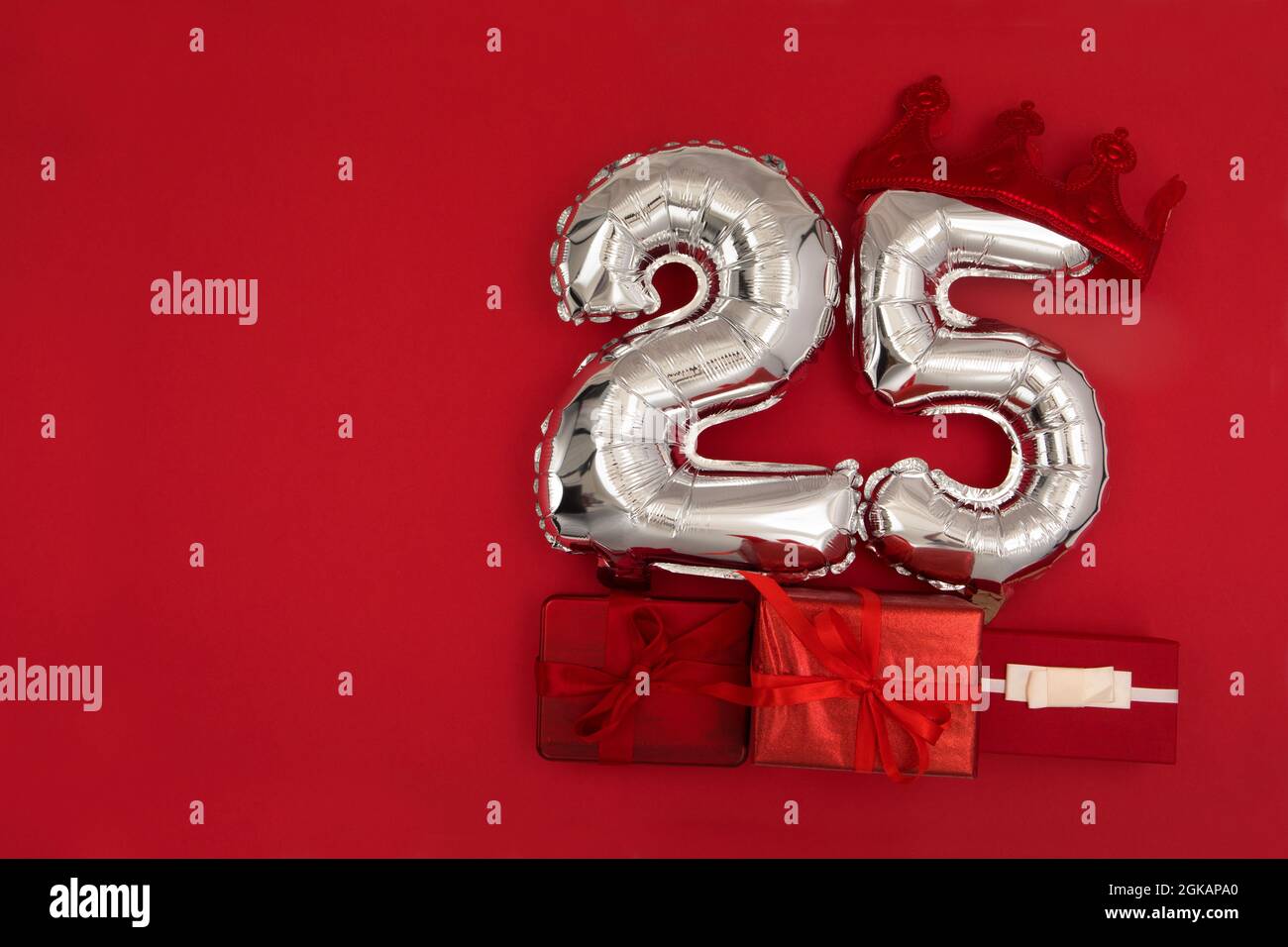 Folie silberne Luftballons mit der Nummer 25 fünfundzwanzig auf rotem Hintergrund mit eingewickelten Geschenken für das Konzept des Geburtstags Stockfoto