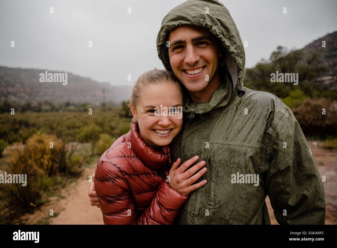 Lächelndes junges, glückliches Trailrunning-Paar, das sich bei Regen und kaltem, bewölktem Wetter vom Berglauf ausruhte Stockfoto