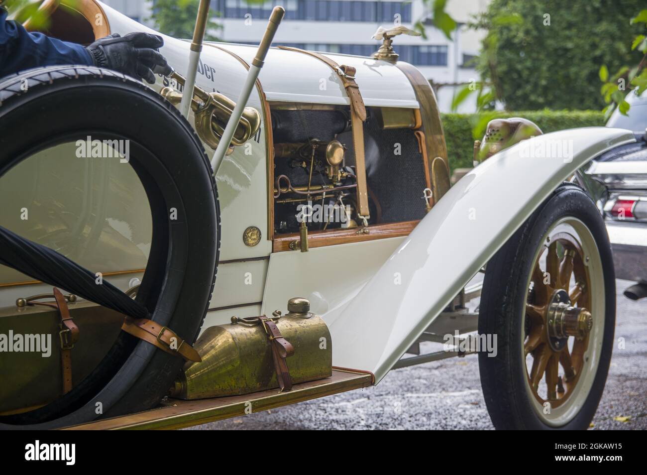 Nahaufnahme des eleganten, raffinierten weißen Goldes antiken Retro-Sportwagens 1914 auf der Ausstellung. Mann fährt in alten Oldtimer-Oldtimer mit Regenschirm, geöffnetem Motor, Holzrädern, kühlem Horn Stockfoto