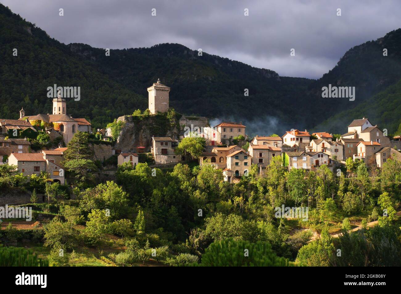Dorf und dunkle umliegende Hügel kurz nach Sonnenaufgang in Peyreleau, Aveyron, Oczitanien, Frankreich Stockfoto