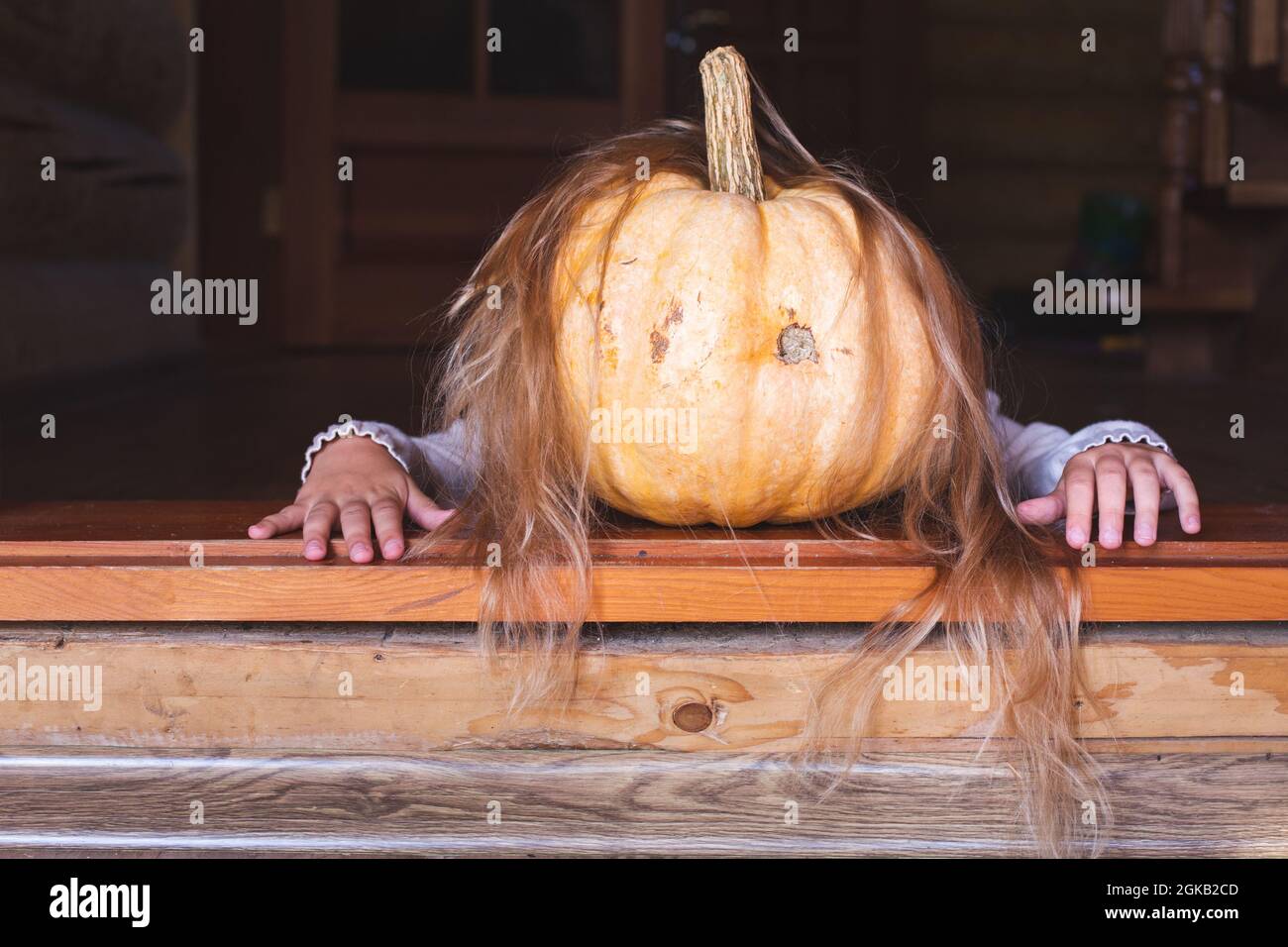 Ein großer orangefarbener Kürbis mit Haaren und Händen kriecht vor der Haustür. Halloween, Herbstferien, Tradition. Gruselige unheimliche Märchenfigur. Kopieren Stockfoto