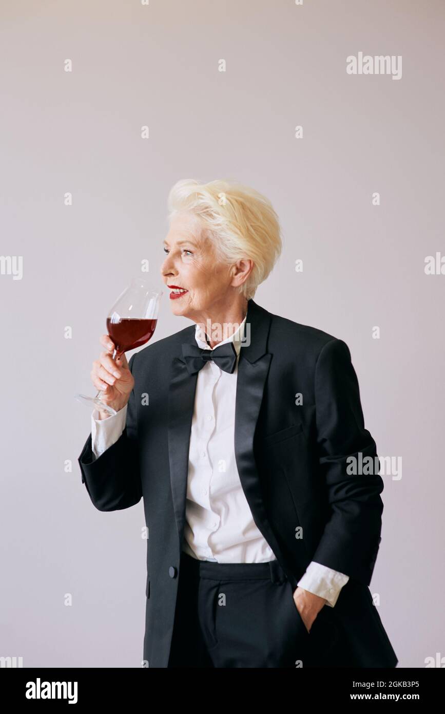 Stilvolle Senior Sommelierin Frau im Smoking mit Glas oder Rotwein. Getränk, ausgereift, Stilkonzept Stockfoto