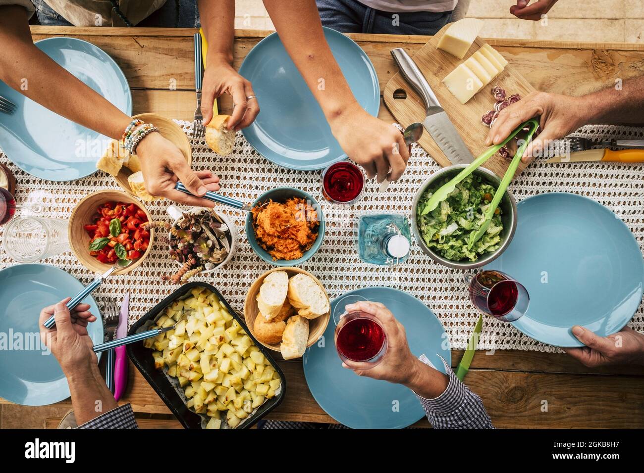 Eine Gruppe von Freunden, die zusammen mit einem Glas Wein auf dem Esstisch essen. Hände, die Lebensmittel aus der Schüssel auf dem Teller nehmen. Gruppe von Menschen genießen Vielfalt an Speisen und Stockfoto