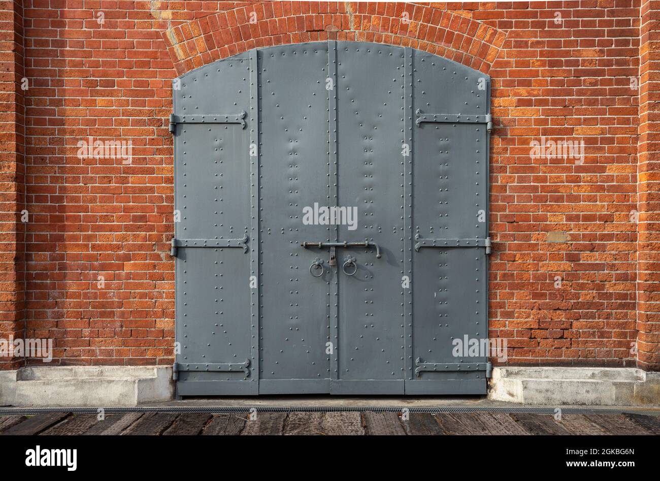 Geschlossenes Eisentor, Tür mit Vorhängeschloss in einem historischen roten Backsteingebäude. Stockfoto
