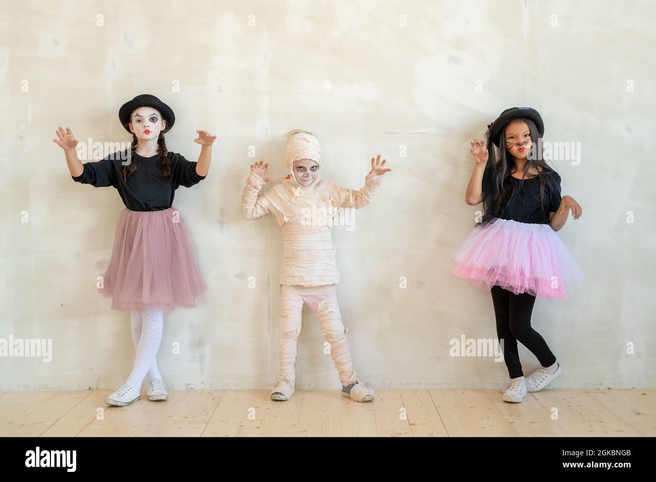 Drei kleine Kinder in halloween-Kleidung stehen an einer weißen Wand vor der Kamera Stockfoto