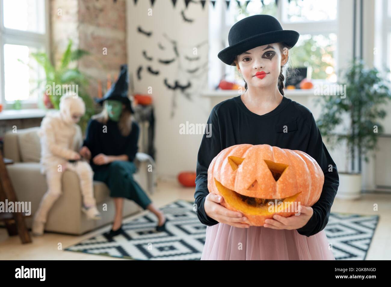 Happy halloween Mädchen in schwarzer Kleidung hält Jack-o-Laterne, während im Wohnzimmer stehen Stockfoto