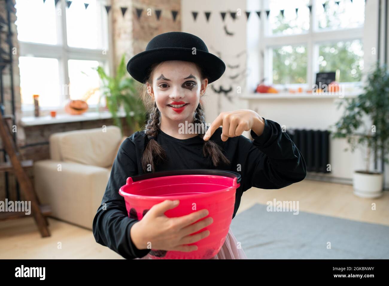 Glückliches Mädchen in schwarzer Kleidung, das vor der Kamera nach Halloween-Leckereien fragt Stockfoto