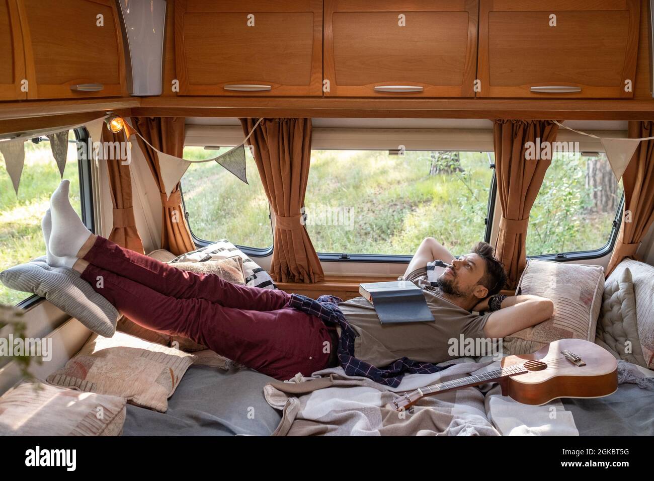 Entspannter junger Mann mit offenem Buch auf der Brust beim Träumen auf dem Bett im Haus auf Rädern Stockfoto