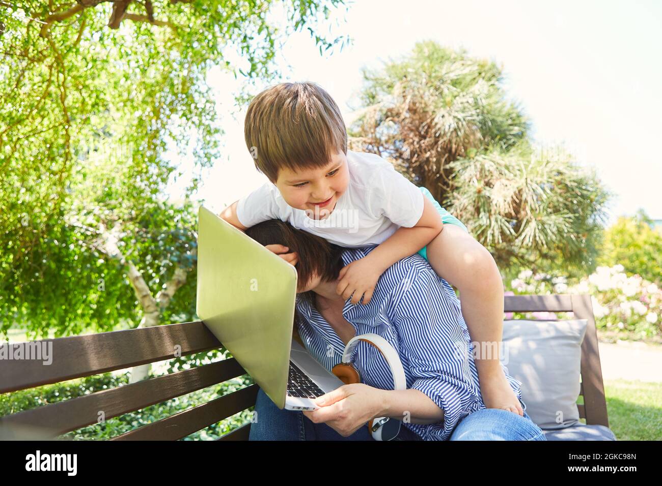 Das Kind stört die Mutter bei der Arbeit am Computer im grünen Garten mit Scheuern Stockfoto