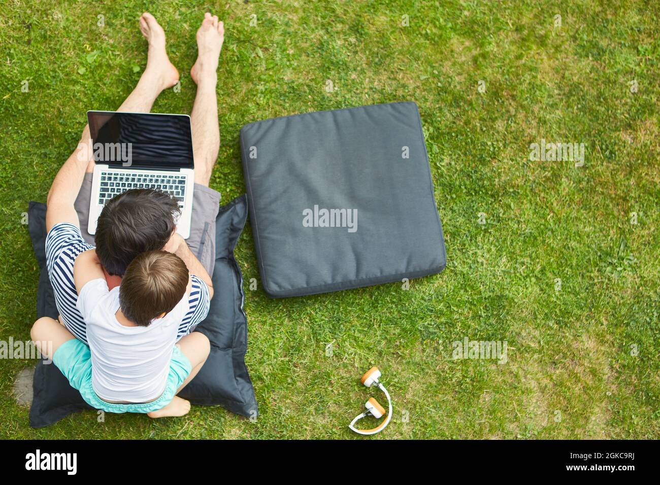 Vater und neugieriger Sohn am Laptop-PC auf dem Rasen im Garten als Heimbüro Stockfoto