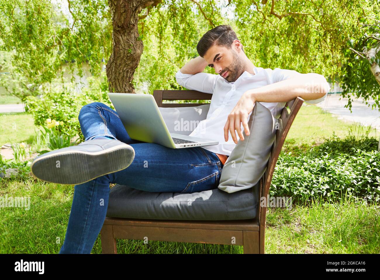 Junger Mann im grünen Garten im Sommer auf dem Laptop als Freiberufler Stockfoto