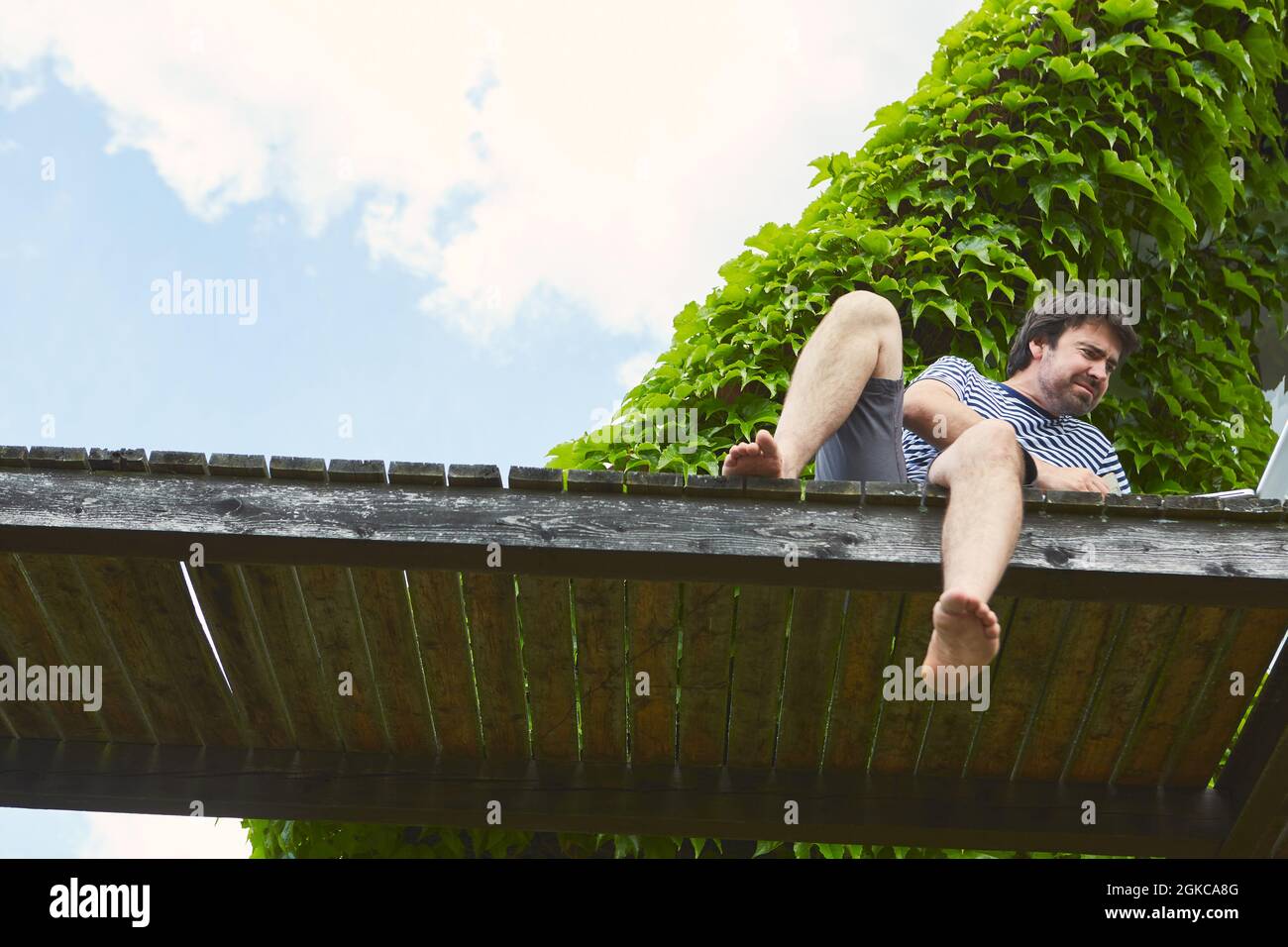 Der Mann auf einem Steg am See arbeitet in den Sommerferien als Freiberufler am Laptop Stockfoto