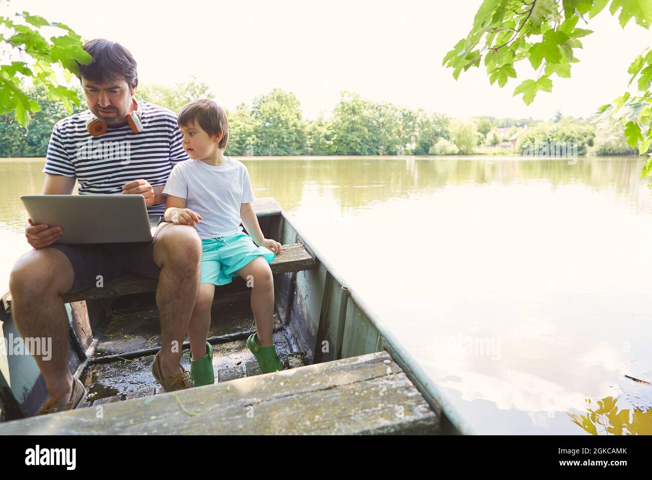 Vater und Sohn benutzen im Sommer als Freiberufler einen Laptop in einem Boot am See Stockfoto