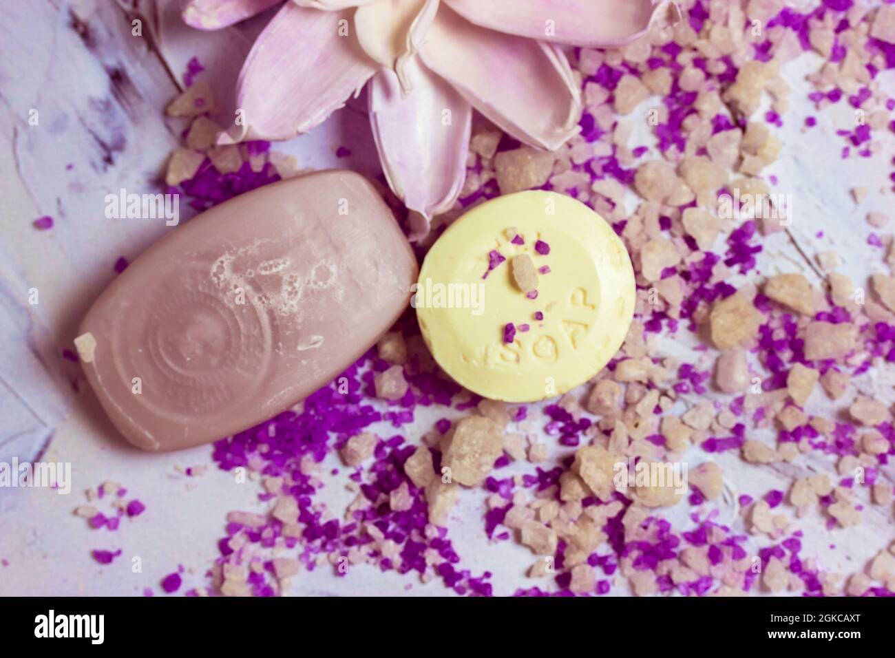 Seifenstücke und eine wunderschöne Lotusblume lagen auf einer weißen Oberfläche, auf der das nach purpurem Lavendel duftende Meersalz zum Baden flach verstreut war. Spa-Behandlungen, entspannen Stockfoto