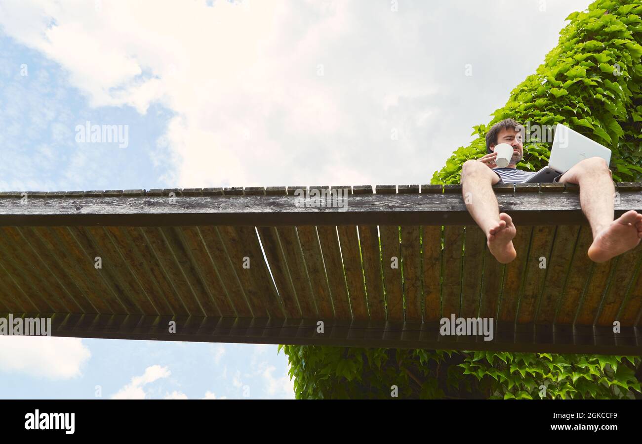 Mann als Freiberufler im Sommer im Urlaub mit Laptop-Computer auf einem Steg am See Stockfoto