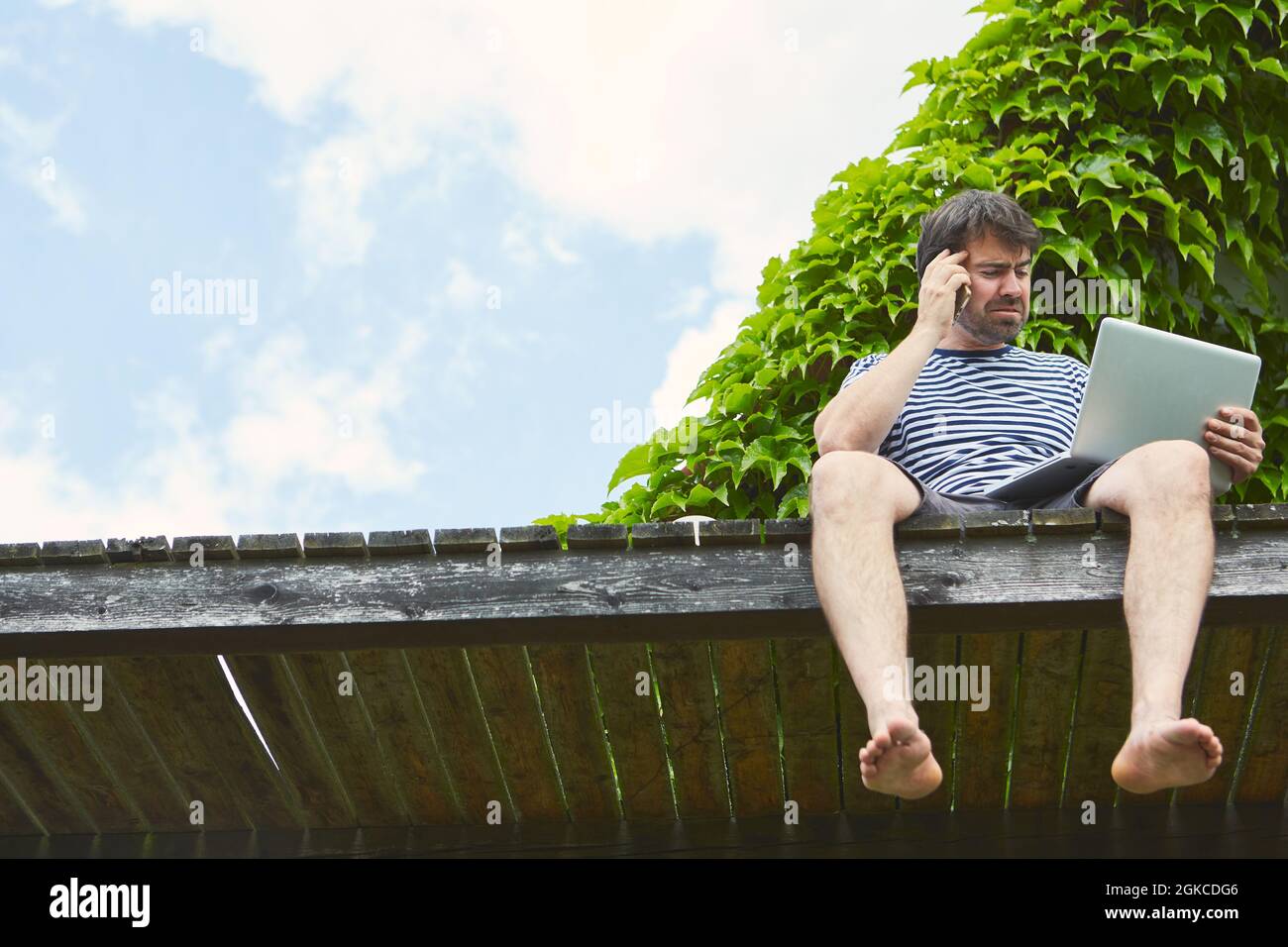 Freiberuflicher Mann im Urlaub auf einem Steg mit Smartphone und Tablet-Computer Stockfoto