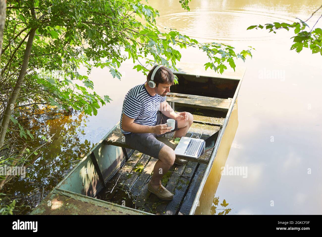 Mann mit einer Tasse Kaffee auf einem Laptop-PC am See in den Sommerferien als Freiberufler Stockfoto