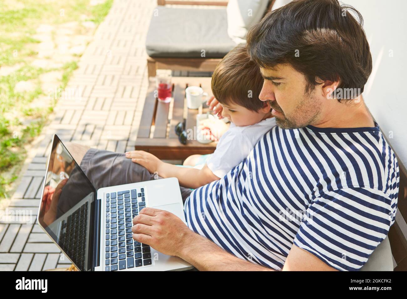Alleinerziehender Vater auf dem Laptop-PC auf der Terrasse zu Hause mit seinem Sohn Stockfoto