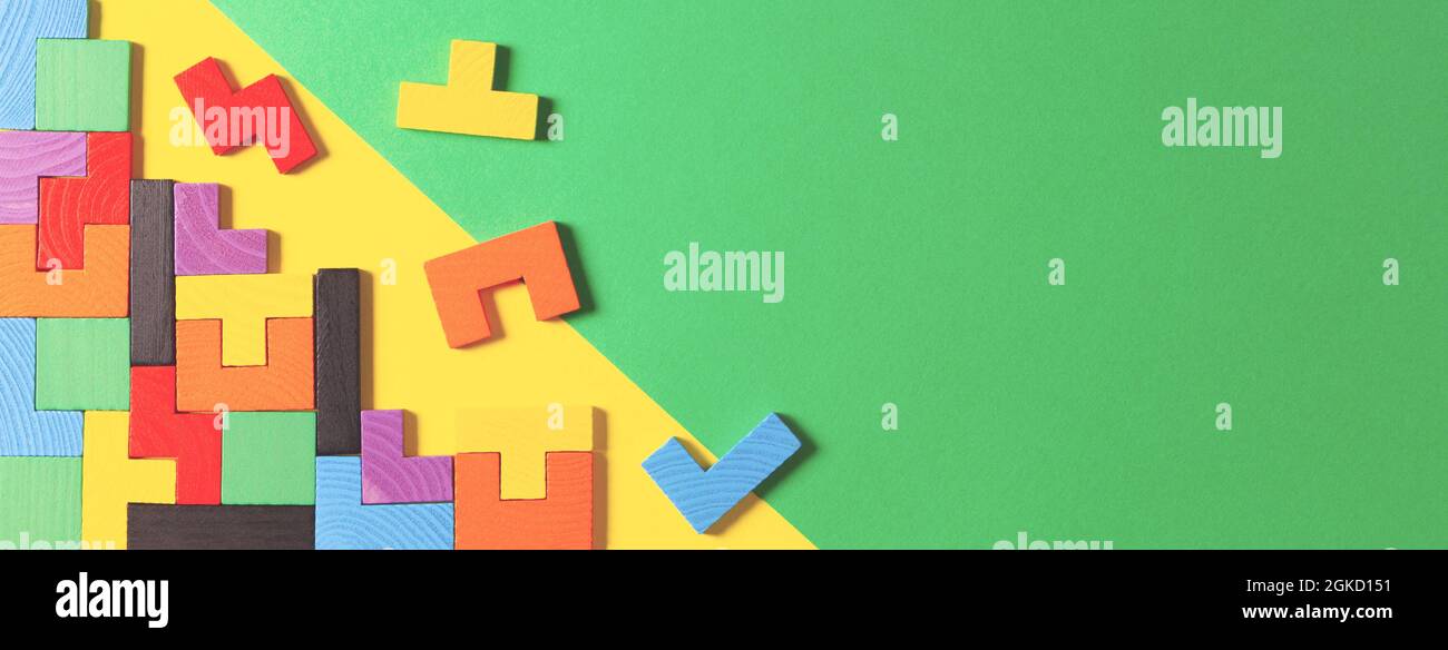 Verschiedene bunte Formen hölzerne Puzzle-Blöcke auf grünem und gelbem Hintergrund. Geometrische Formen in verschiedenen Farben, Draufsicht Stockfoto