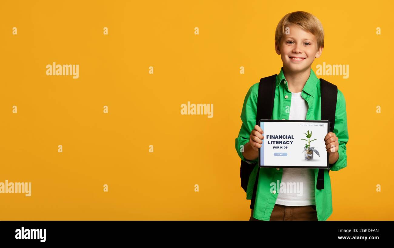 Fröhlicher Junge demonstriert Tablet-Computer mit Financial Literacy for Kids Online-Schule-Website auf orangefarbenem Hintergrund Stockfoto