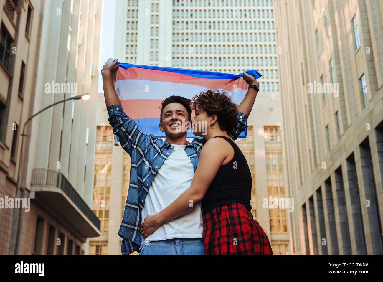 Geschlecht nicht konformen Paar feiert Homosexuell Stolz im Freien. Glückliches junges queeres Paar, das die Transgender-Flagge hochhebt, während es in der Stadt steht. Junge LG Stockfoto