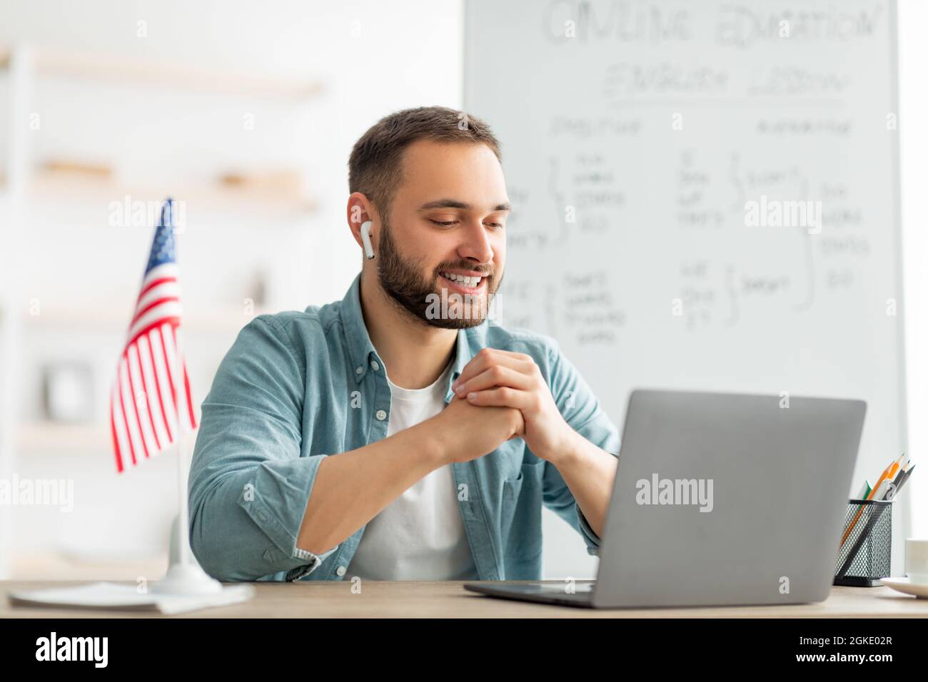 Glücklicher männlicher Lehrer, der Englischunterricht im Internet mit einem Laptop im Heimbüro gibt. Modernes Fernschulungskonzept Stockfoto
