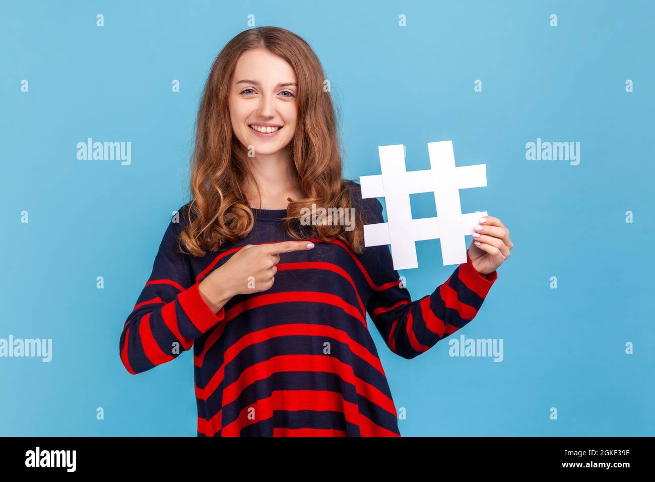 Attraktive Frau mit welligen Haaren im Pullover, die auf weißen Hashtag, trendige Social-Media-Posts und Blogging, virale Web-Inhalte, Internetwerbung zeigt. I Stockfoto