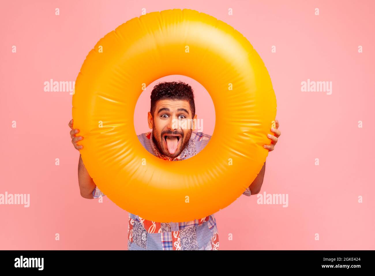 Portrait von brünett bärtig verrückt aufgeregt Mann hält orange Gummiring in den Händen, Blick auf die Kamera mit lustigen Ausdruck, zeigt Zunge aus. Indoo Stockfoto