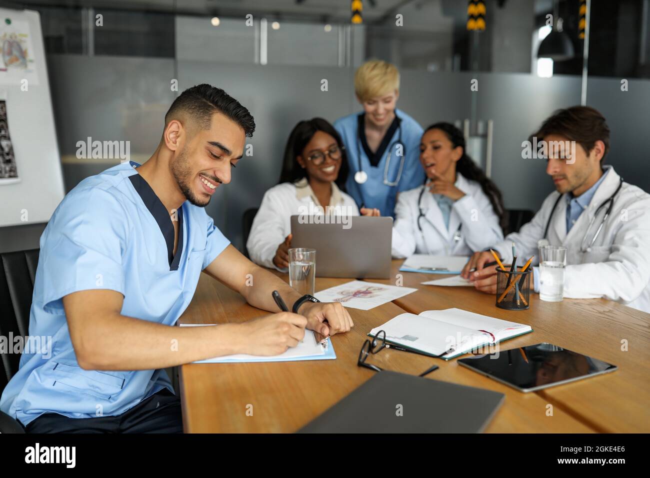 Freundliches multiethnisches Ärzteteam, das am Tisch sitzt und einen Laptop benutzt Stockfoto