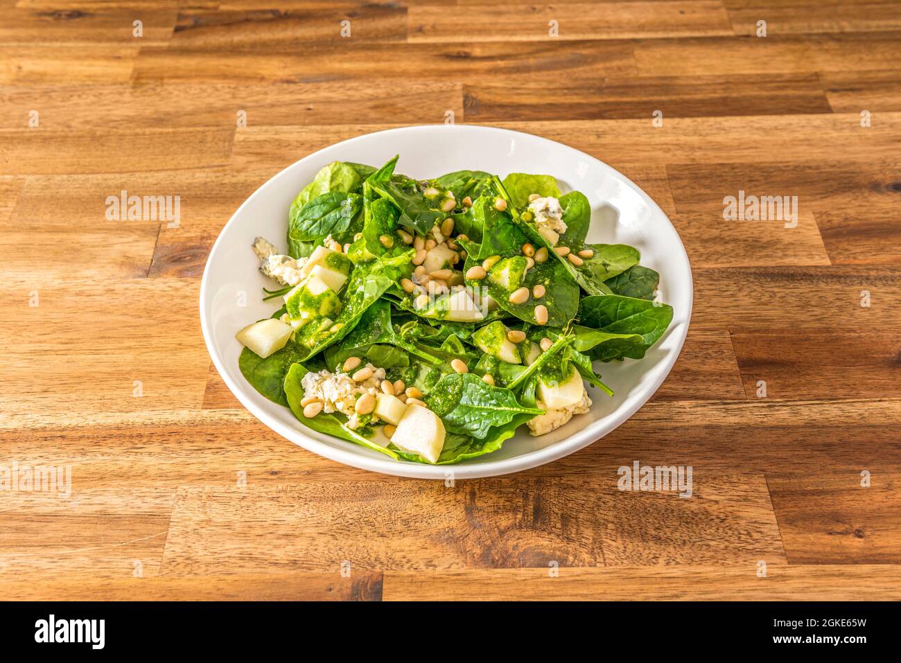 Spinatsalat mit gehackten Birnen, Menge Pinienkerne und Blauschimmelkäse in einer weißen Schüssel Stockfoto