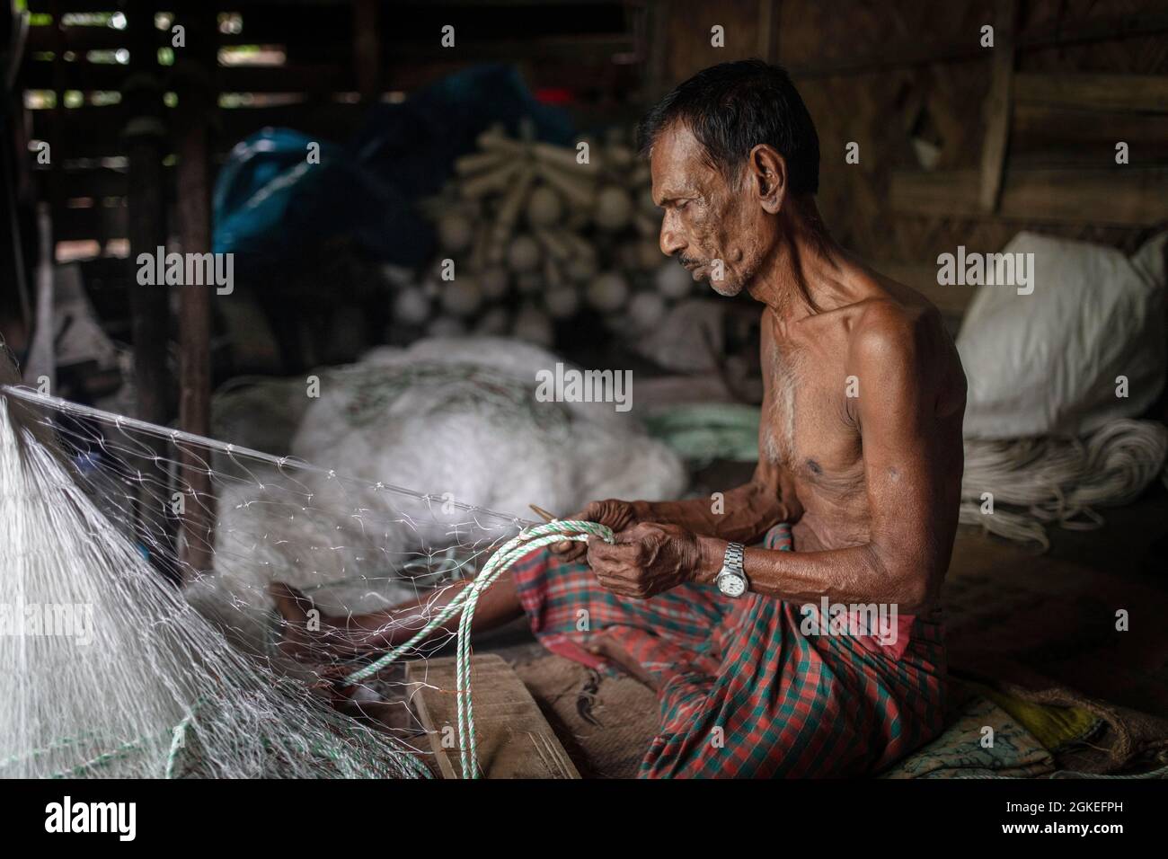 Ein Fischer sitzt auf dem Boden seiner Hütte und repariert ein Fischernetz, Mongla, Sundarbans, Bangladesch Stockfoto