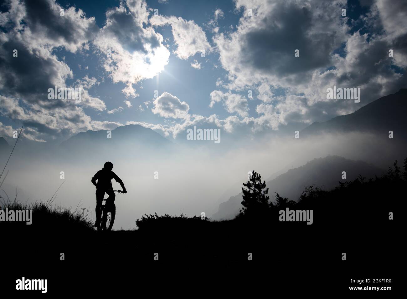 Ein Mann fährt mit einem E-Bike Mountainbike bergauf in der Nähe des alpinen Dorfes Sambuco, Cuneo, Piemont, Italien. Silhouette. E-Bike. Stockfoto