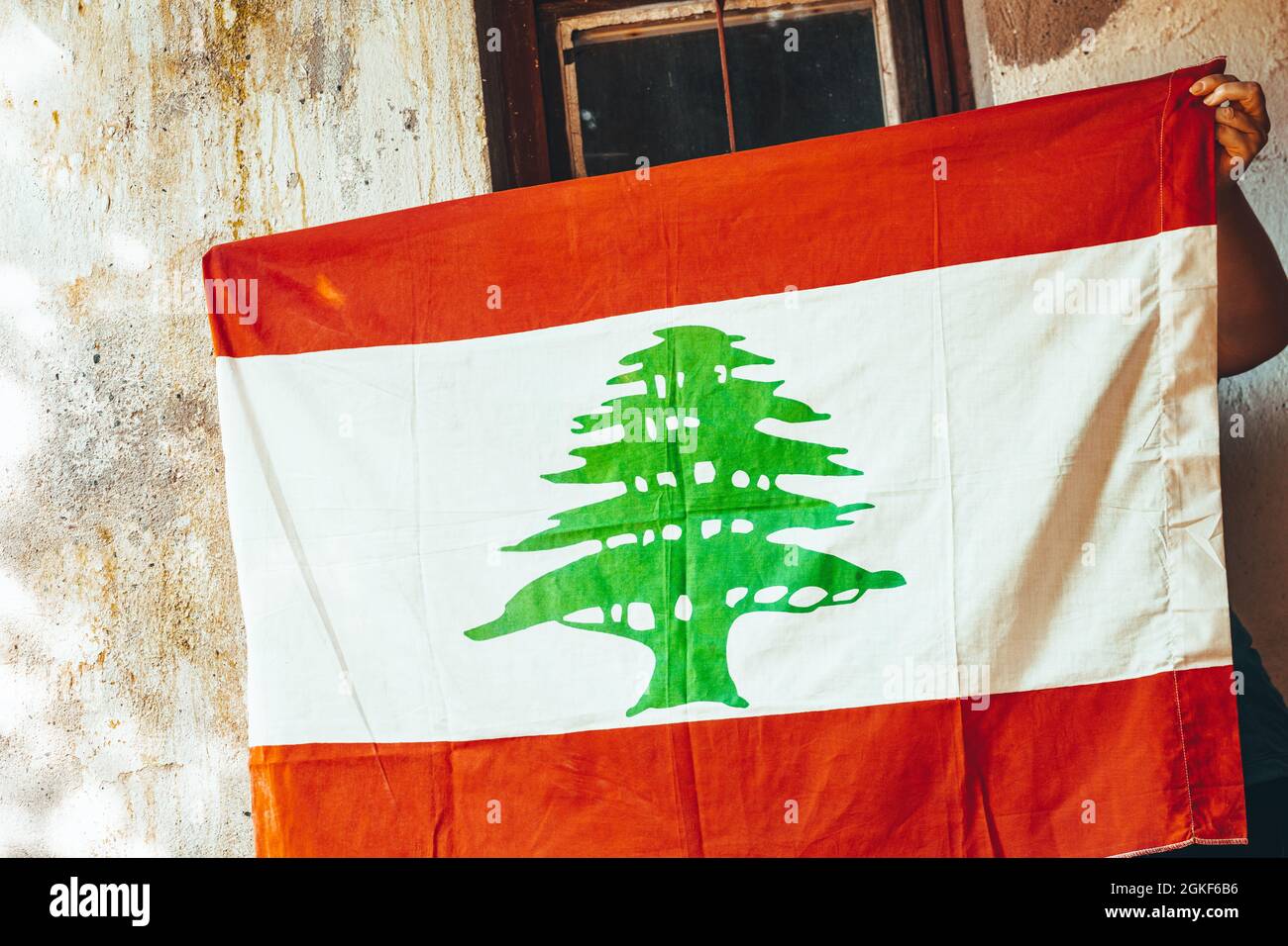 Eine große libanesische Flagge breitete sich vor dem Hintergrund einer alten schäbigen Mauer aus Stockfoto