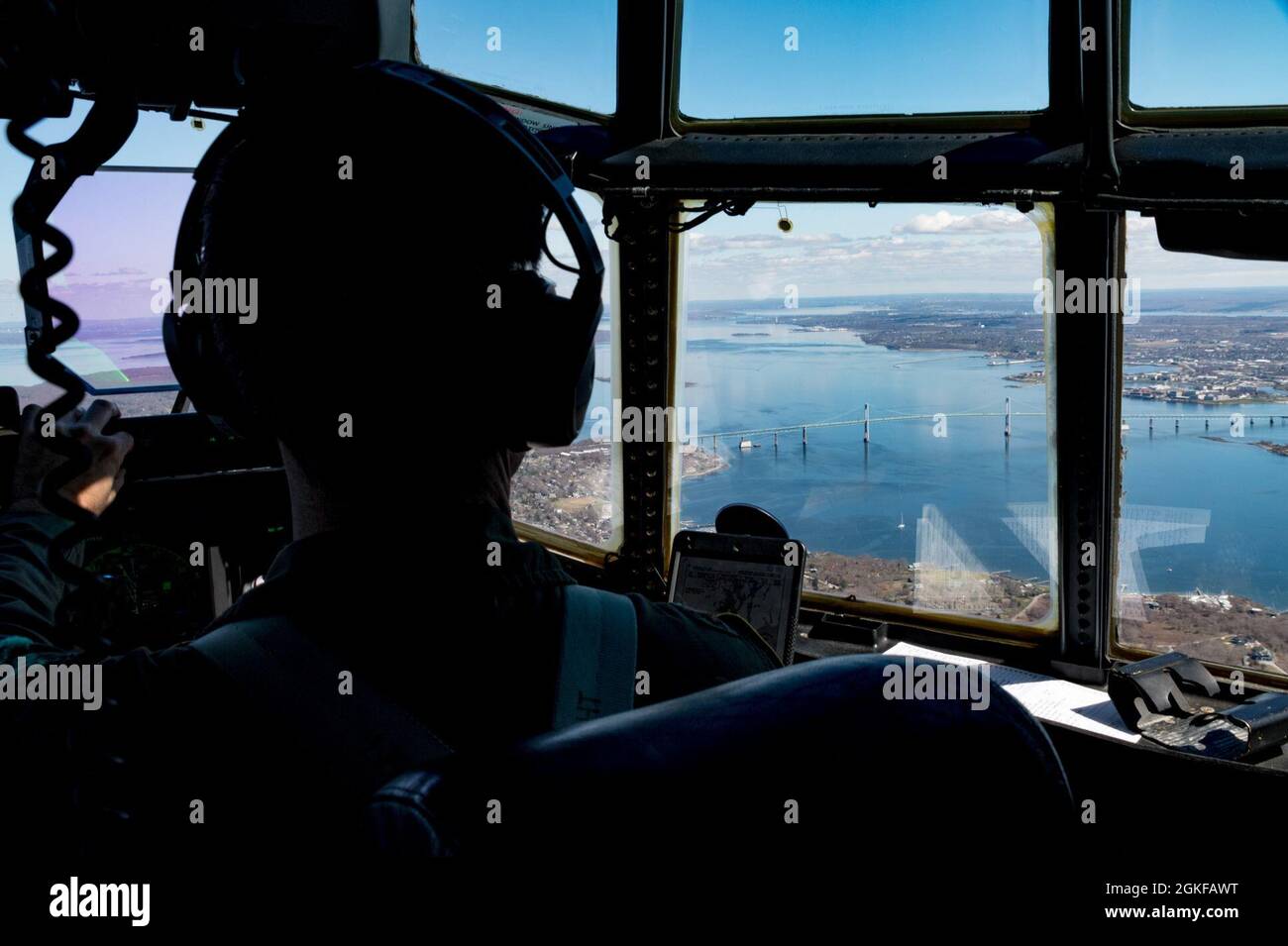 Air National Guard Maj. Ian Friel, ein C130J Hercules Pilot vom 143d Airlift Wing, schaut heraus, wie das Flugzeug über die Claiborne Pell Newport Bridge, 7. April 2021, über Narragansett Bay, R.I., hindurchfährt Friel, die Luftbesatzung der 143 AW und der U.S. Special Operations Forces, haben sich zusammengetan, um hochgelegene Fallschirmsprünge mit geringer Öffnung durchzuführen. Die C-130 kann schnell für die verschiedenen Ladungstypen umkonfiguriert werden, wie z. B. palettierte Geräte, bodenbeladenes Material, Fallbühnen, Container-Liefersystembündel, Fahrzeuge und Personal oder aeromedizinische Evakuierung. Stockfoto