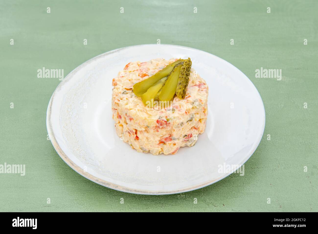 Spanische Tapa aus russischem Salat mit Gurken auf weißem Teller und grünem Tisch Stockfoto