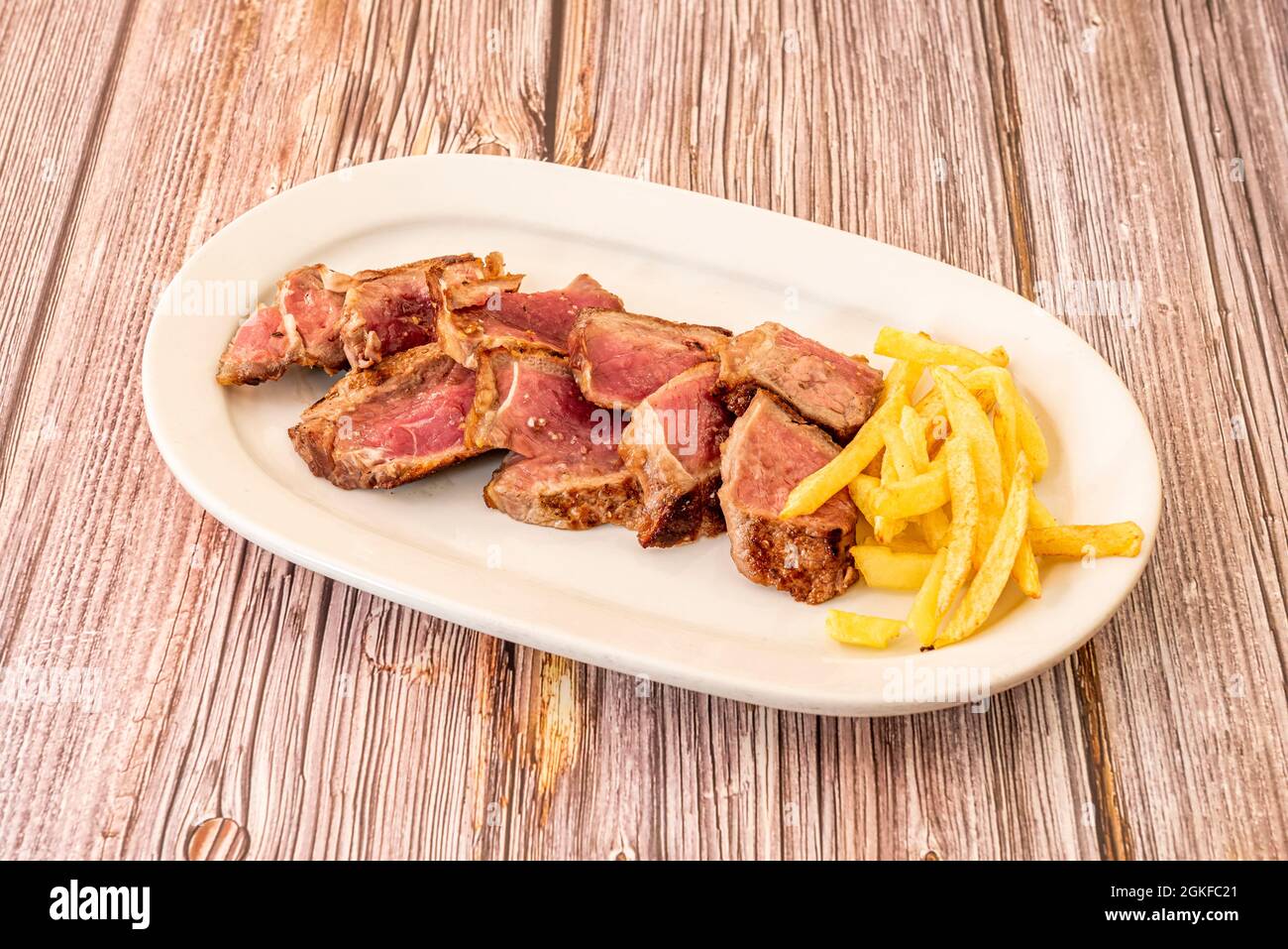 Rindfleisch-Entrecote bis auf den Punkt gekocht und mit einer Garnierung von hausgemachten Chips auf einem weißen Tablett gefüllt Stockfoto