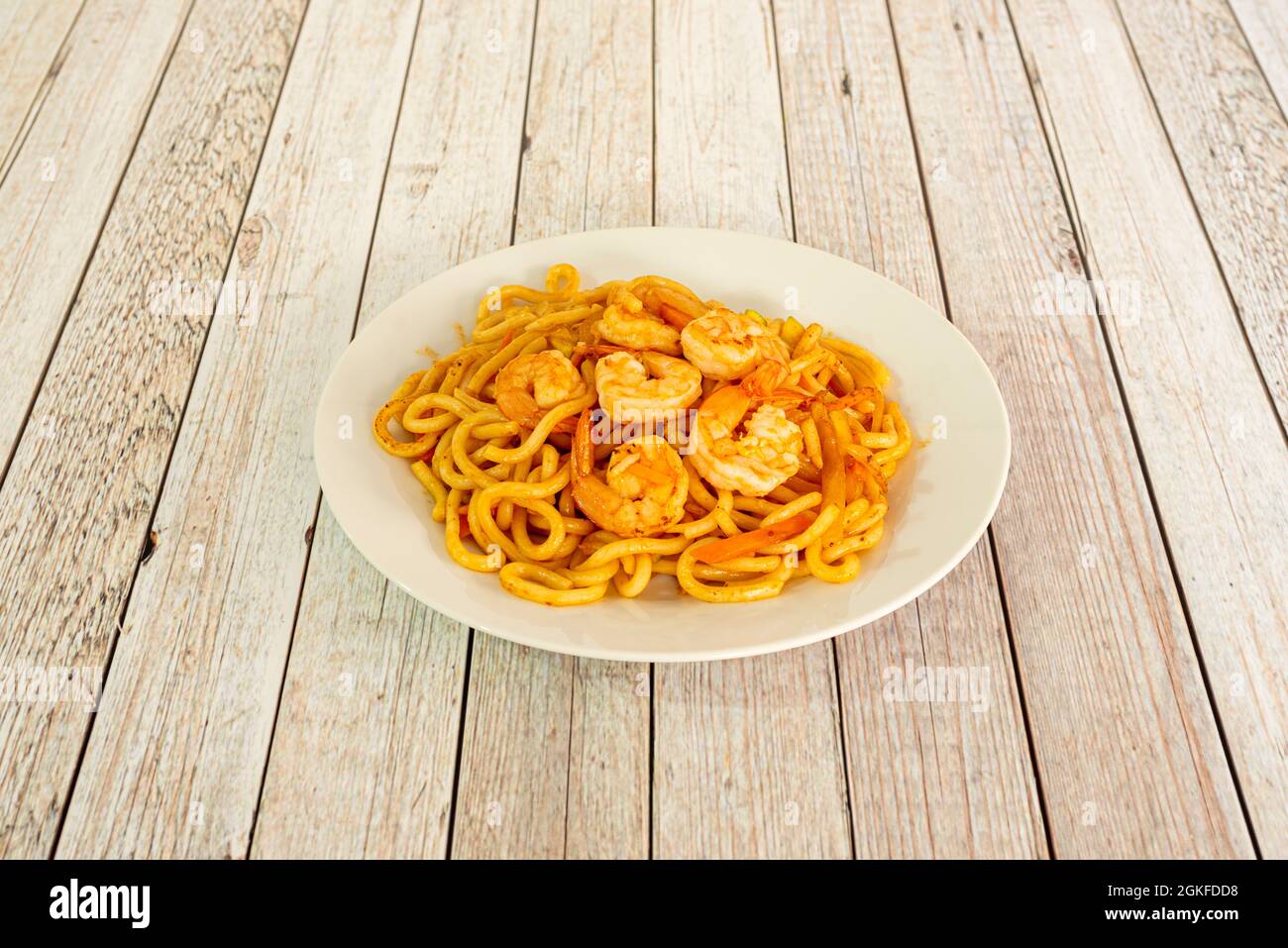 Gebratene udon-Nudeln mit geschälten Garnelen und Wok-sautiertem Gemüse auf weißem Teller Stockfoto