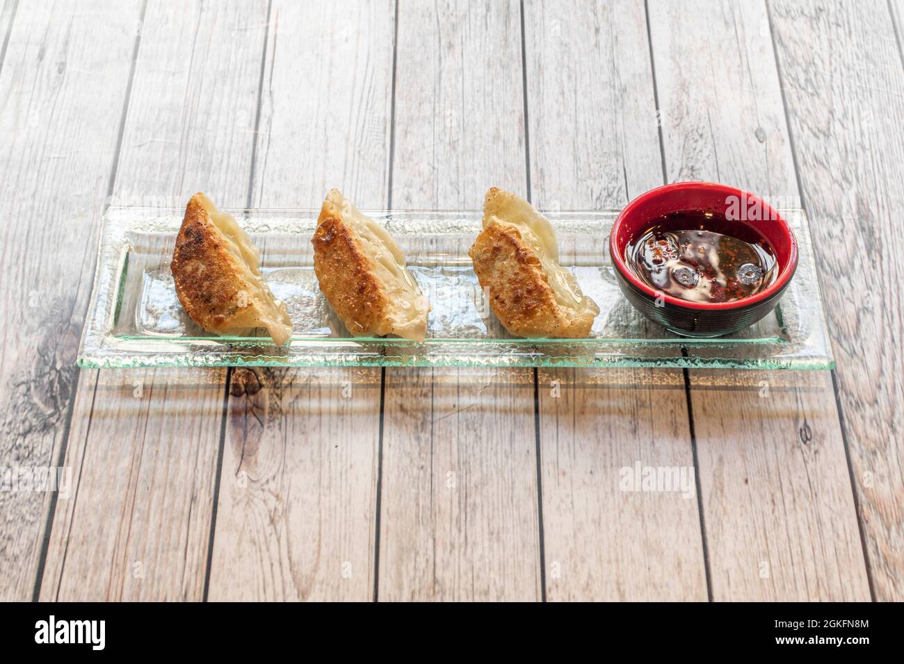 Glastablett mit einer Portion japanischer Knödel, Gyozas, mit einem Behälter mit Sojasauce auf der Seite Stockfoto